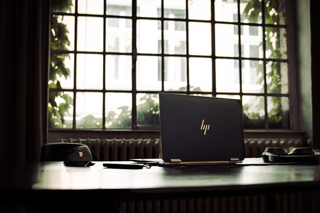 Desk with an open laptop, notebook and plant near a window